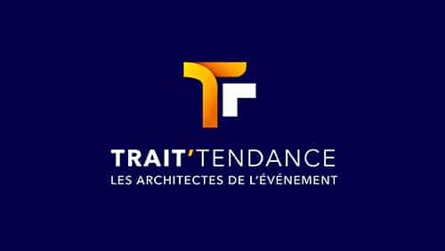 Logo pour "TRAIT'TENDANCE" avec le slogan "LES ARCHITECTES DE L'ÉVÉNEMENT" sur un fond bleu foncé, avec un "T" stylisé orange et blanc au-dessus du texte.