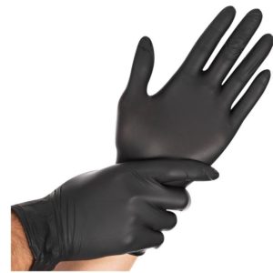 Une personne portant un gant noir jetable à une main et tirant sur un second gant noir avec l'autre main.