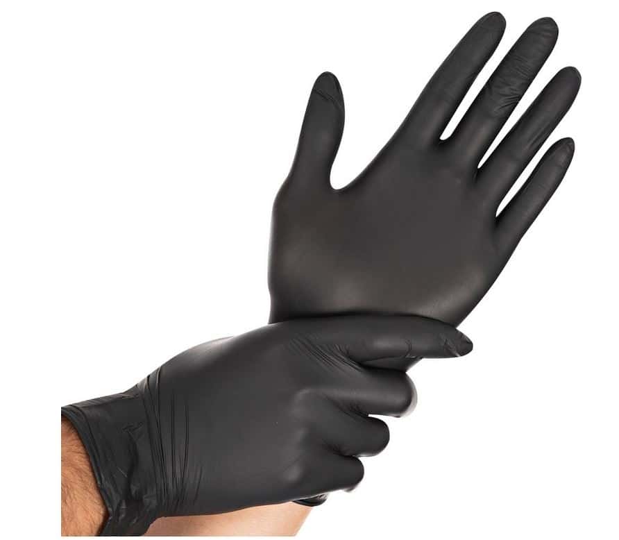 Une personne portant un gant noir jetable à une main et tirant sur un second gant noir avec l'autre main.