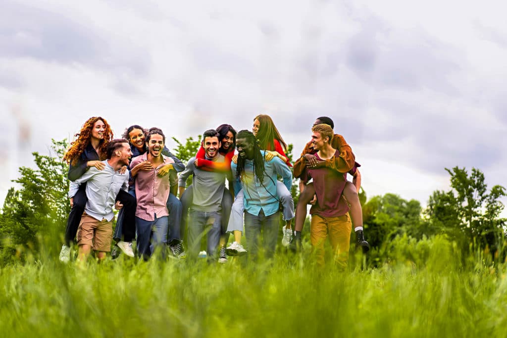 Un groupe de jeunes adultes riant et se promenant à dos d'âne en plein air sur un terrain herbeux avec des arbres en arrière-plan, embrassant la responsabilité sociétale et environnementale tout en profitant de la nature ensemble.