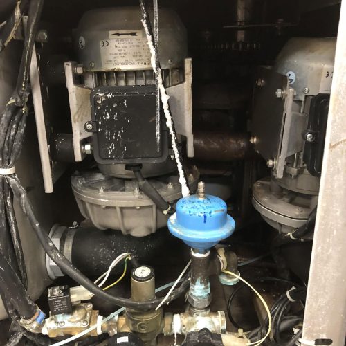 Vue rapprochée d'une machine industrielle avec un câblage, deux moteurs, une vanne bleue, des tuyaux et un manomètre. Les résidus de liquide et la corrosion sur les composants mettent en évidence l'importance des services de nos pour un entretien adéquat.
